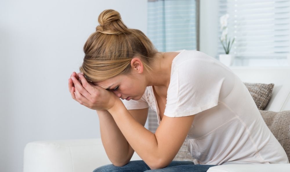 Mujer tomándose la cara con las manos sufriendo de amnesia, despersonalización y desrealización producto de la disociación por trauma