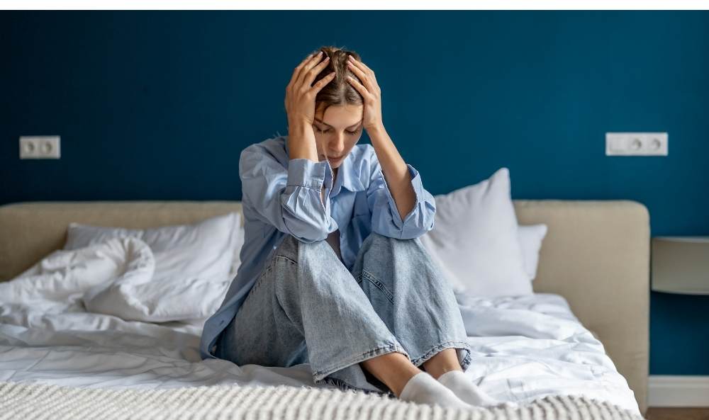 Mujer en la cama tomándose la cabeza como sintoma de su trauma complejo