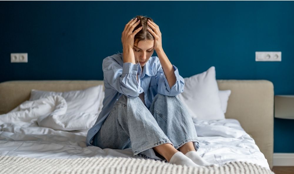 Mujer sentada en la cama con las manos en la cabeza productod traumas simples y complejos que la aquejan